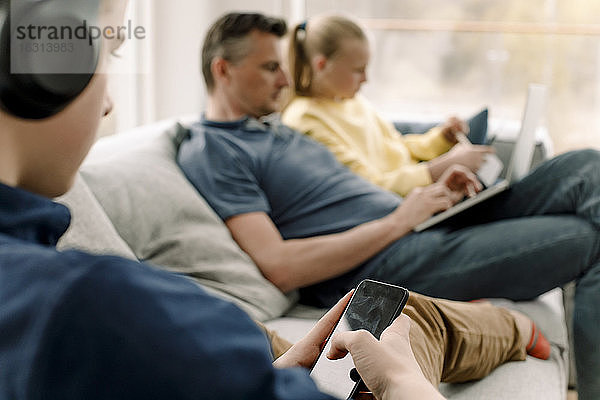 Teenager benutzt Smartphone  während er mit seiner Familie auf dem Sofa sitzt