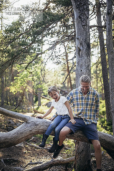 Glücklicher Vater und Tochter ziehen auf umgefallenen Baum im Wald
