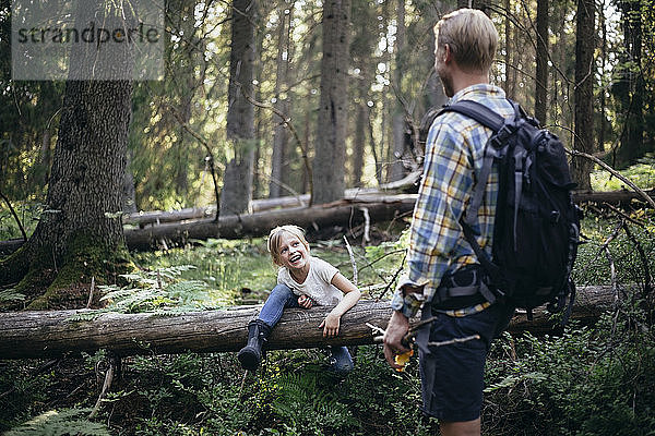 Lächelnde Tochter klettert über umgefallenen Baum  während sie den Vater im Wald anschaut