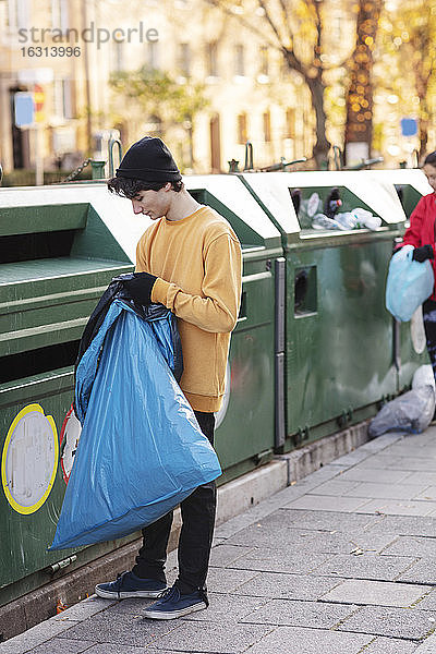 Junge männliche und weibliche Freiwillige werfen Plastikabfälle in den Mülleimer