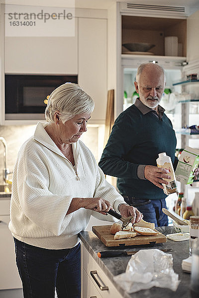 Ältere Frau bereitet Essen zu  während der männliche Partner ein Getränk in der Küche hält