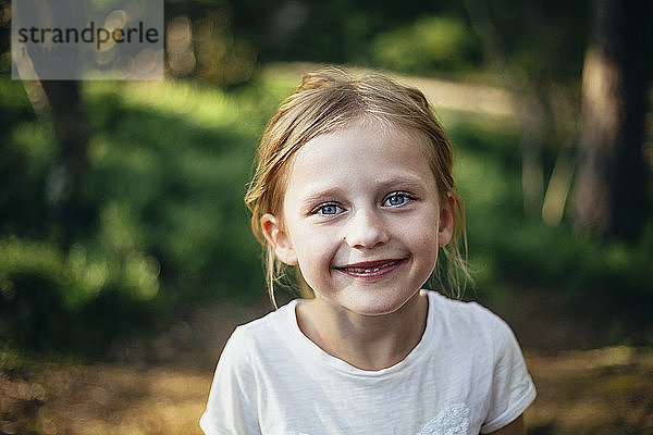 Porträt eines niedlichen lächelnden Mädchens im Wald stehend