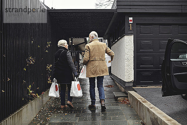 Rückansicht eines älteren Paares mit Taschen  die im Winter gemeinsam auf dem Bürgersteig gehen