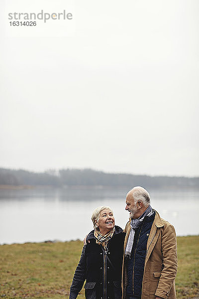 Lächelndes älteres Paar schaut sich an  während es am See vor klarem Himmel steht