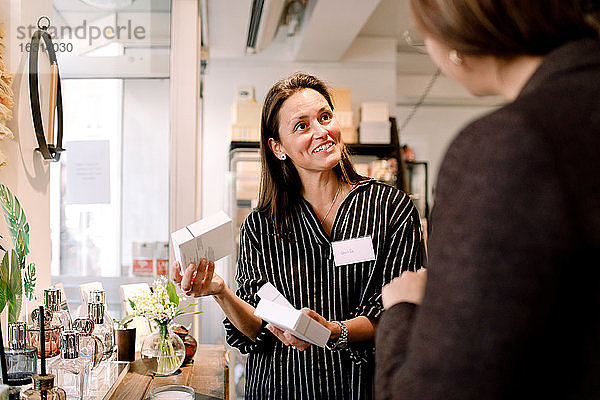 Lächelnde Verkäuferin mit Parfümschachtel im Gespräch mit Kunden im Geschäft