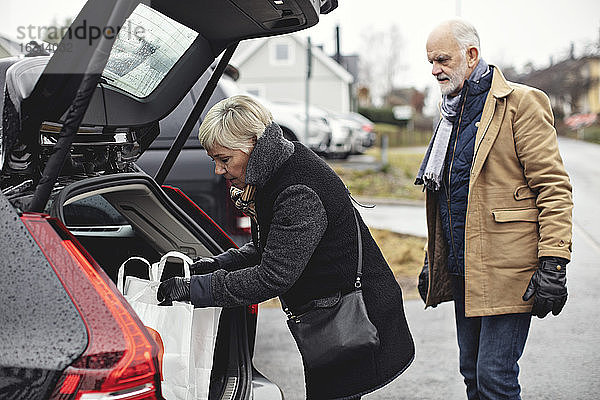 Älterer Mann schaut auf Partner  der im Winter am Kofferraum des Autos steht