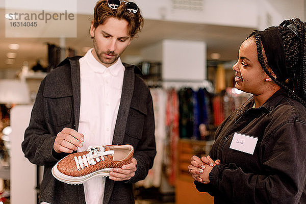 Lächelnde Verkäuferin zeigt einem männlichen Kunden im Einzelhandel einen Schuh