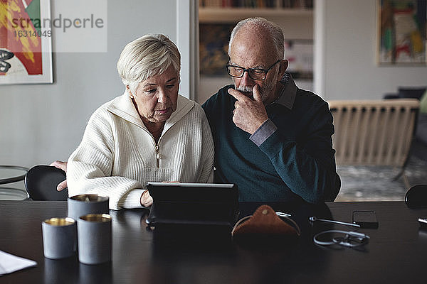 Älteres Ehepaar benutzt digitales Tablett  während es am Esstisch im Wohnzimmer sitzt