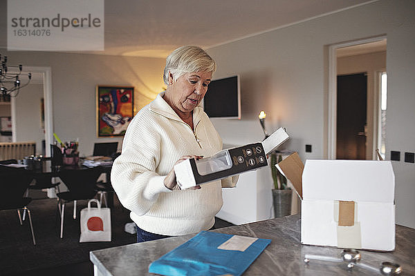 Zerknitterte ältere Frau packt Kiste über Kücheninsel aus