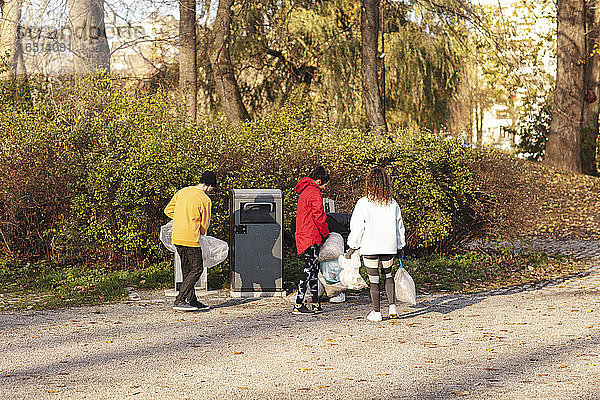 Junge männliche und weibliche Umweltschützer halten Abfälle an der Mülltonne