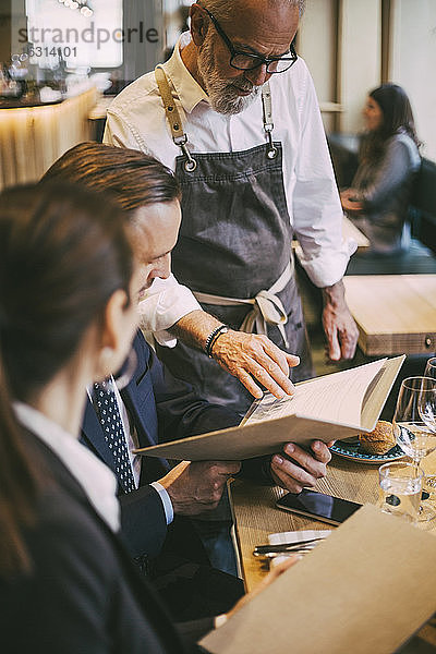 Kellner am Tisch stehend  während Geschäftsleute im Restaurant sitzen