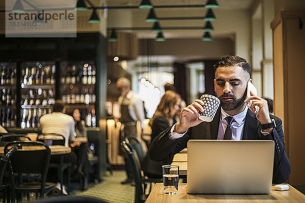 Geschäftsmann telefoniert beim Kaffeetrinken im Restaurant