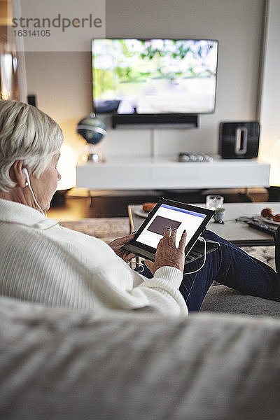 Ältere Frau benutzt digitales Tablet  während sie auf dem Sofa im Wohnzimmer sitzt