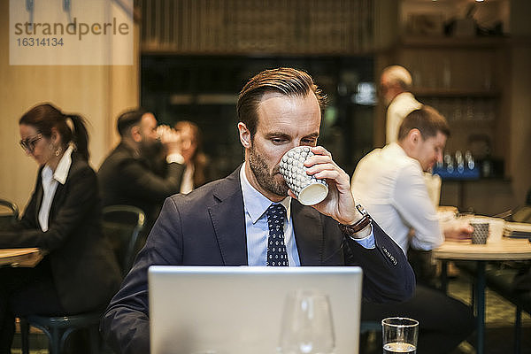 Männlicher Unternehmer arbeitet am Laptop  während er im Restaurant Kaffee trinkt