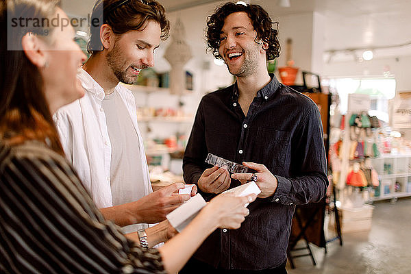 Lächelnde männliche Freunde im Gespräch mit einer Verkäuferin im Geschäft