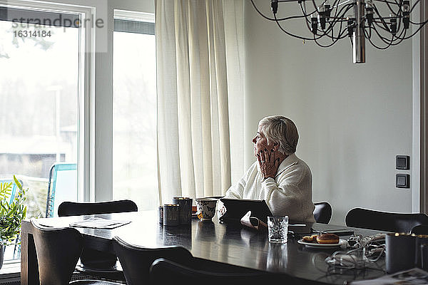 Ältere Frau schaut weg  während sie zu Hause am Esstisch sitzt