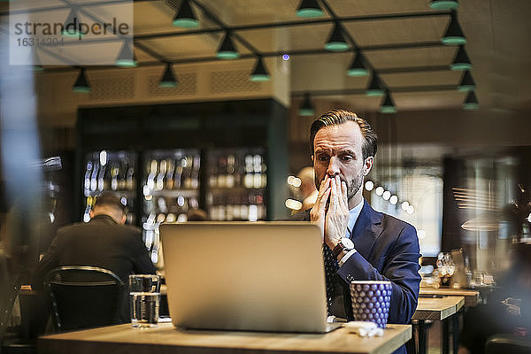 Besorgter Geschäftsmann schaut auf Laptop im Restaurant