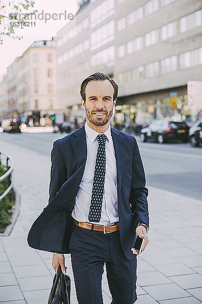 Porträt eines Geschäftsmannes mit Tasche und Telefon beim Spaziergang in der Stadt