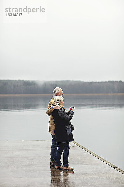 Älteres Ehepaar in voller Länge am See vor klarem Himmel stehend