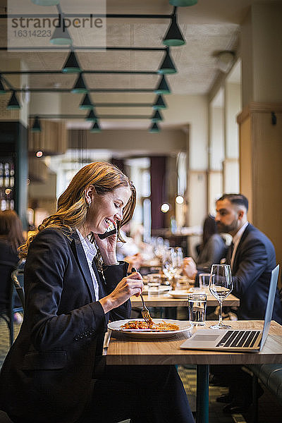 Lächelnde Geschäftsfrau telefoniert beim Essen im Restaurant