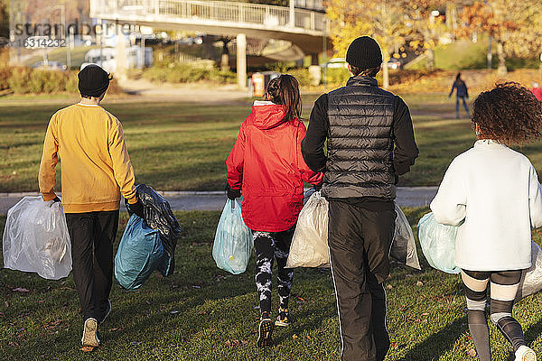 Rückansicht von jungen Umweltschützern  die mit Plastikmüll im Park spazieren