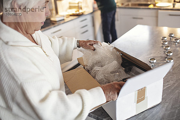Seitenansicht einer älteren Frau beim Auspacken des Kartons auf der Kücheninsel zu Hause