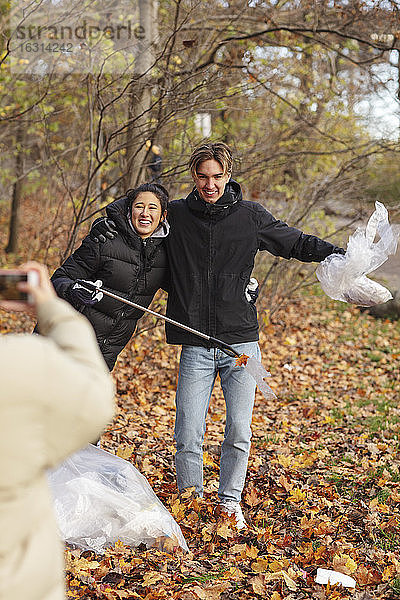 Junge Umweltschützerin fotografiert lächelnde Freunde  die im Park Mikroplastik halten