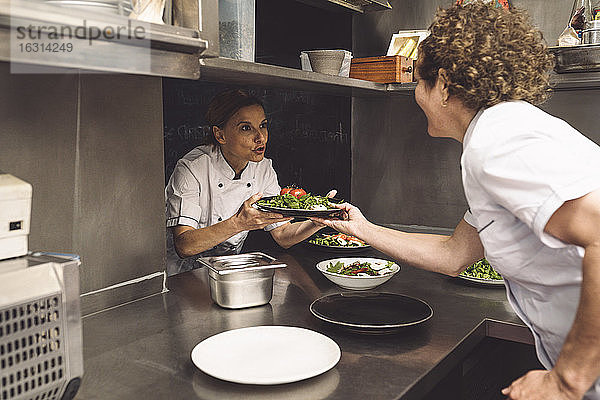 Köchin im Gespräch mit einer Mitarbeiterin beim Verteilen von Speisen in einer Großküche