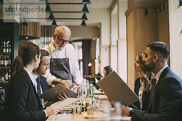 Kellner zeigt Geschäftsleuten im Restaurant die Speisekarte