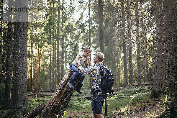 Vater hält Tochter über Baumstamm im Wald