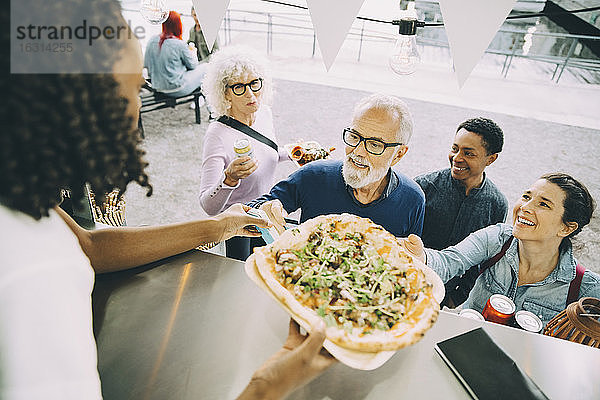 Junge Besitzerin gibt glücklichen männlichen und weiblichen Kunden Essen