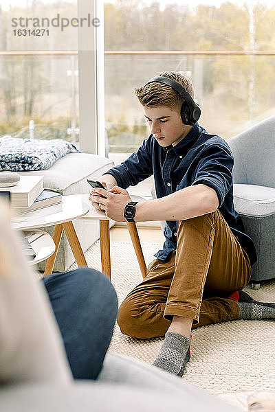 Teenager benutzt Mobiltelefon  während er zu Hause auf dem Boden sitzt
