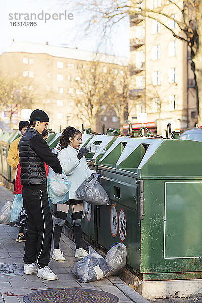 Junge männliche und weibliche Umweltschützer werfen Abfall in den Mülleimer