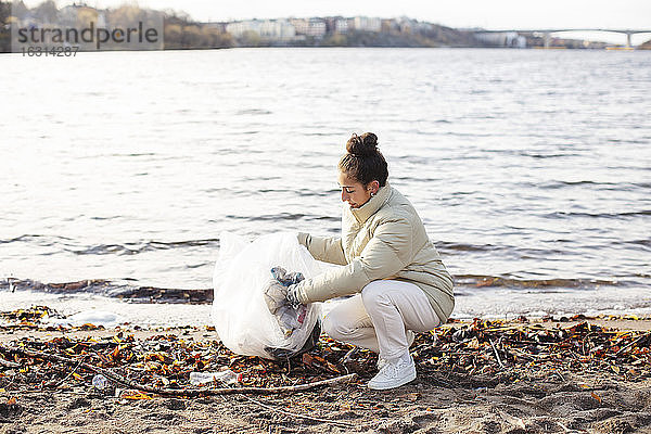 Junge Umweltschützerin sammelt Abfall  während sie am See kauert