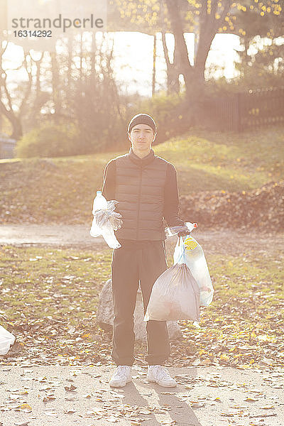 Porträt eines jungen männlichen Freiwilligen mit Plastikmüll im öffentlichen Park stehend