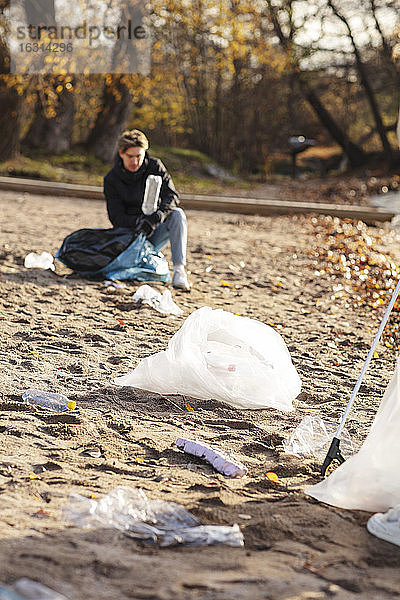 Männlicher Umweltschützer sammelt auf Sand verstreute Kunststoffe auf