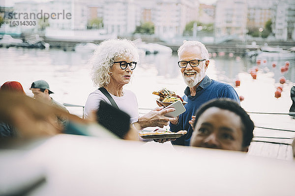 Lächelnde männliche und weibliche Kunden genießen indisches Essen in der Stadt