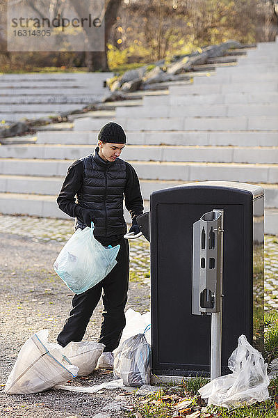 Männlicher Umweltschützer mit Plastikmüll an der Mülltonne