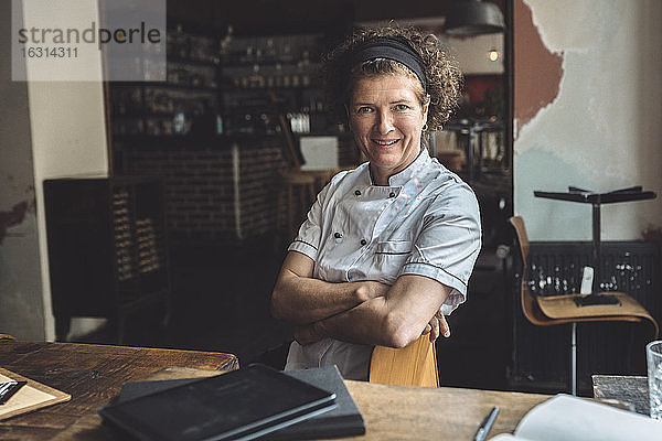 Porträt eines lächelnden reifen Kochs mit verschränkten Armen im Restaurant