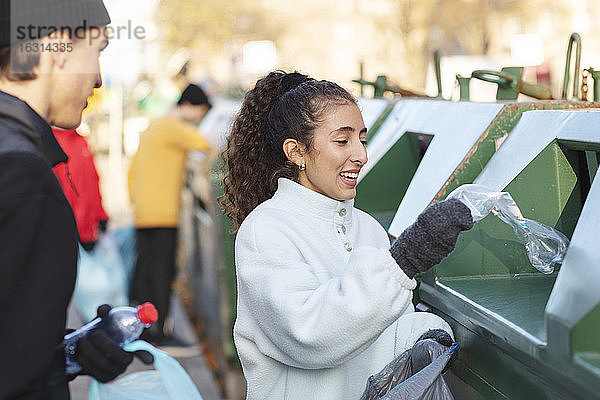 Lächelnde Umweltschützerin mit Freundin  die Abfall in den Mülleimer wirft