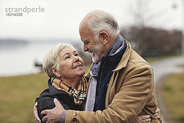 Lächelndes älteres Paar umarmt sich am See