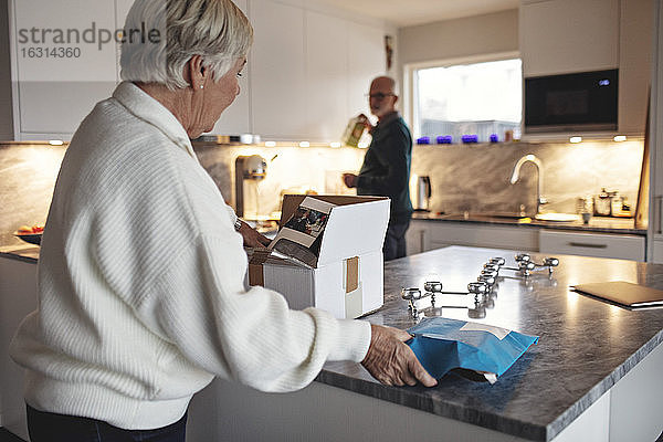 Seitenansicht einer älteren Frau beim Auspacken des Kartons über der Kücheninsel