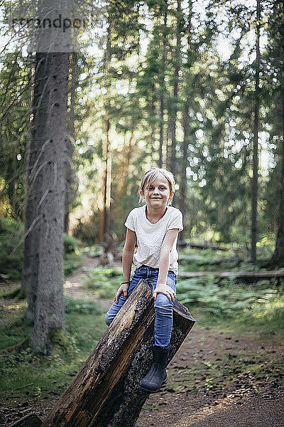 Porträt einer lächelnden Tochter auf einem Baumstamm im Wald sitzend