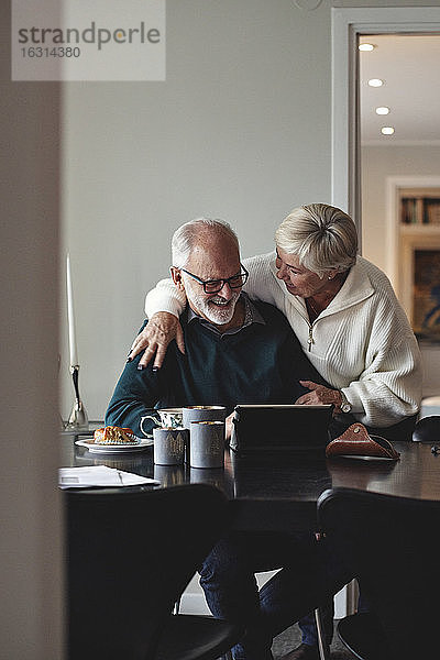 Lächelndes älteres Paar beim Gespräch am Esstisch im Wohnzimmer