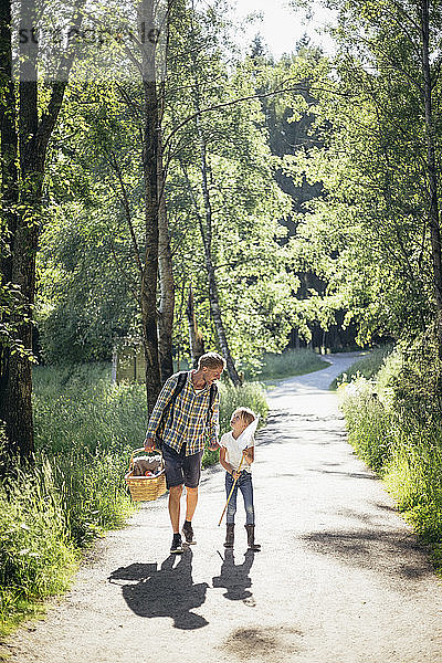 Tochter spricht mit Vater  der einen Picknickkorb auf der Straße im Wald hält