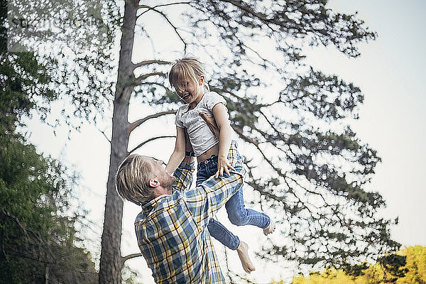 Glücklicher Vater hält Tochter in der Luft gegen Bäume