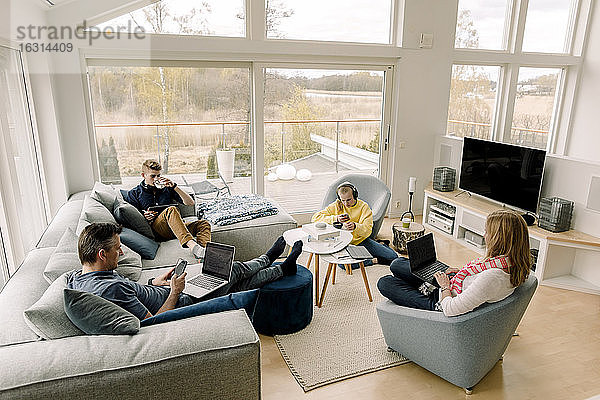 Hochwinkelansicht einer Familie unter Verwendung von Technologie beim Sitzen im Wohnzimmer