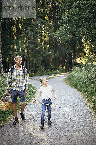 Lächelnde Tochter im Gespräch mit Vater  der einen Picknickkorb auf der Straße im Wald hält