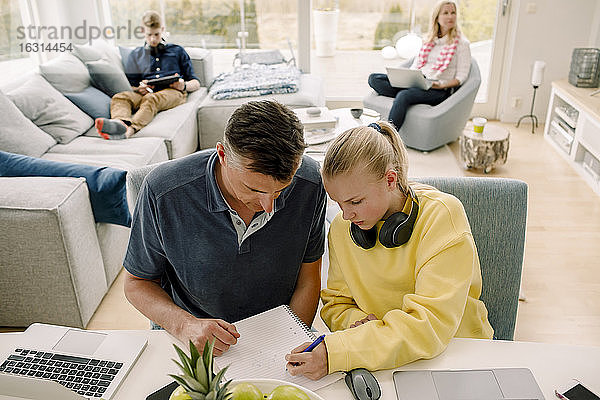 Hochwinkelaufnahme eines Vaters  der seine Tochter unterrichtet  während er im Wohnzimmer am Tisch sitzt