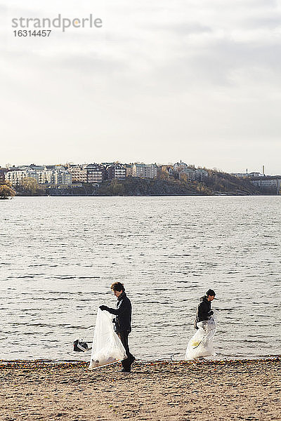 Junge männliche Umweltschützer sammeln Plastikabfälle am See bei klarem Himmel